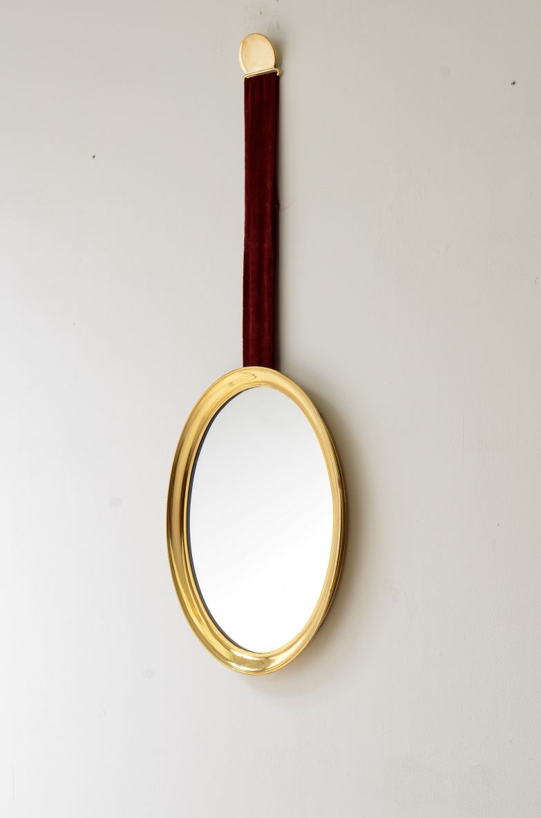 Mirror in shaped brass hanging from an original velvet ribbon and fixed to the wall using a brass disc.  Italian manufacture, 1950s/60s.