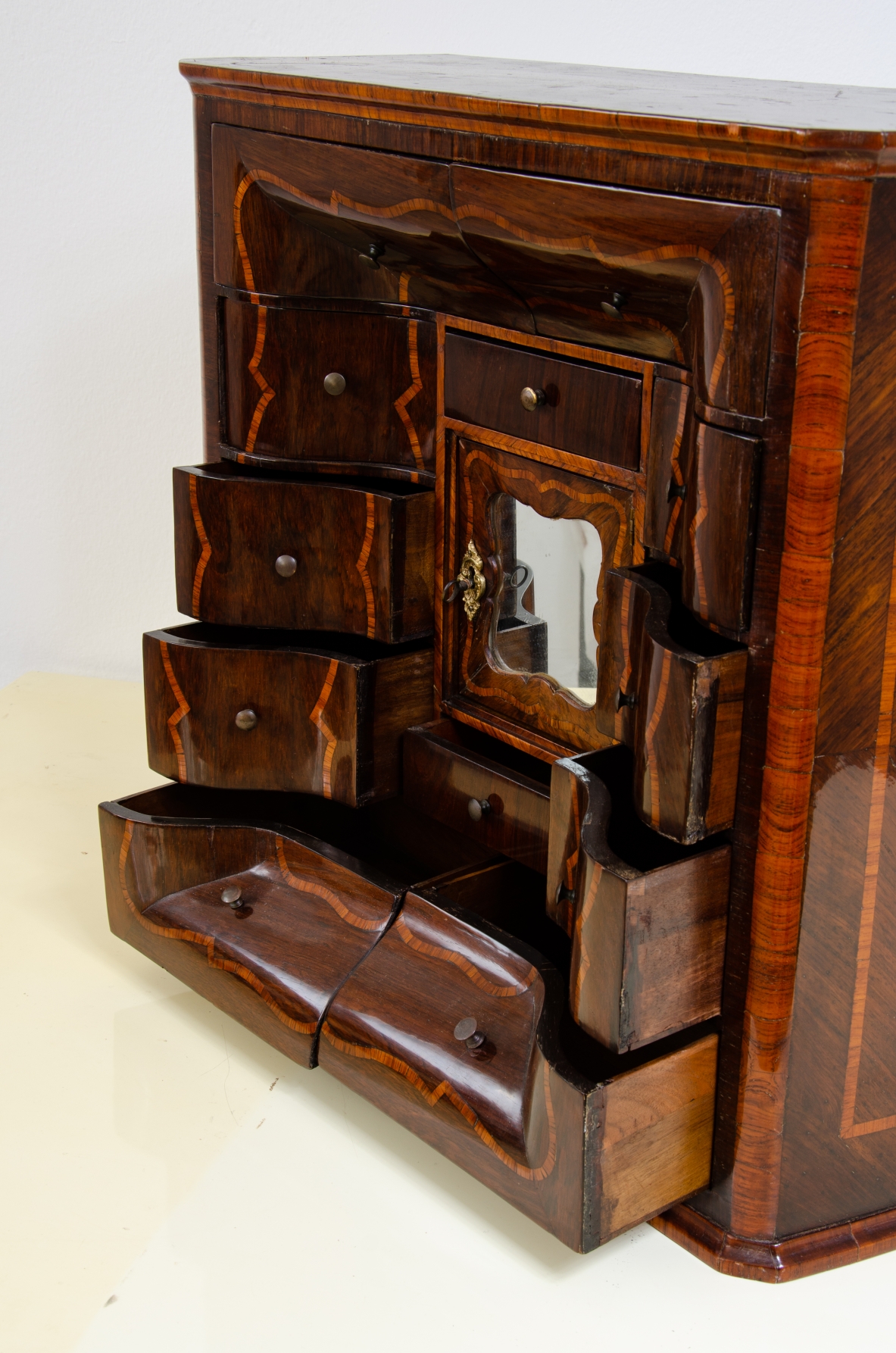Genoese cabinetry, c. 1750, coin cabinet in violet wood threaded in rose wood with wavy front, central aedicule with shaped door and central mirror.