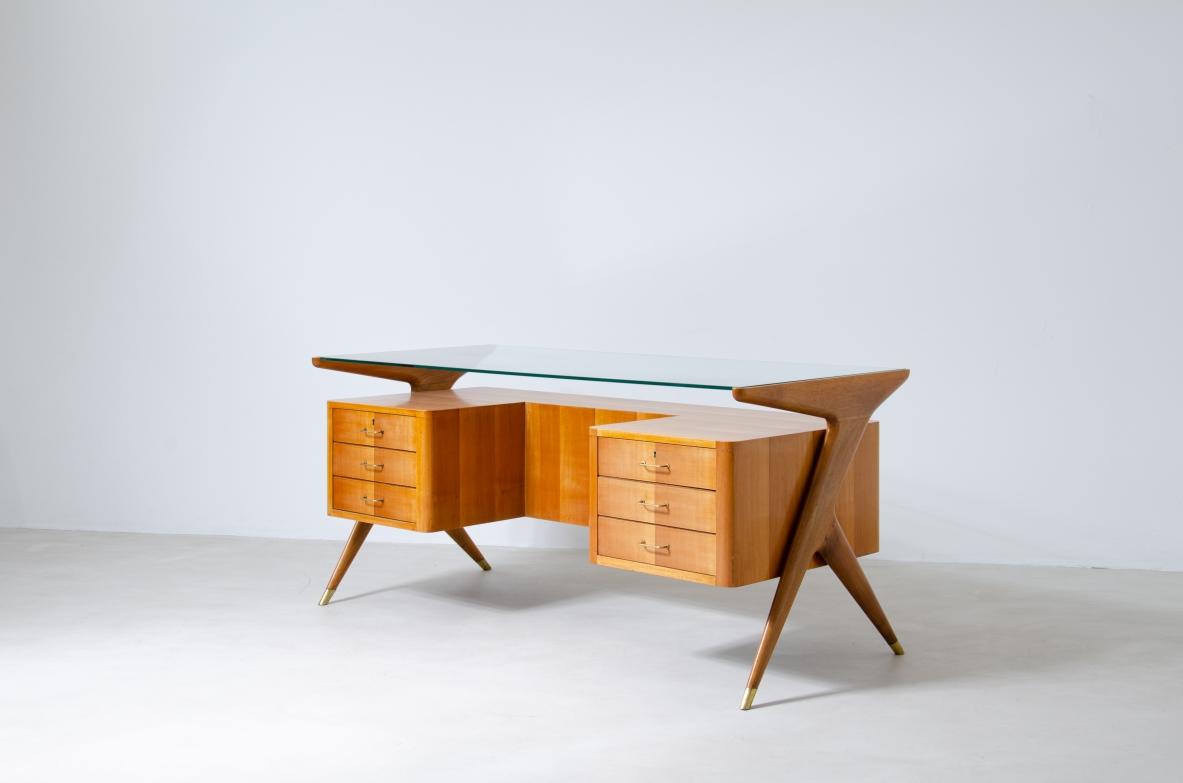 Scrivania in legno biondo con piano in vetro di grande spessore e montanti laterali sagomati con puntali in ottone,.  Manifattura italiana 1950ca.