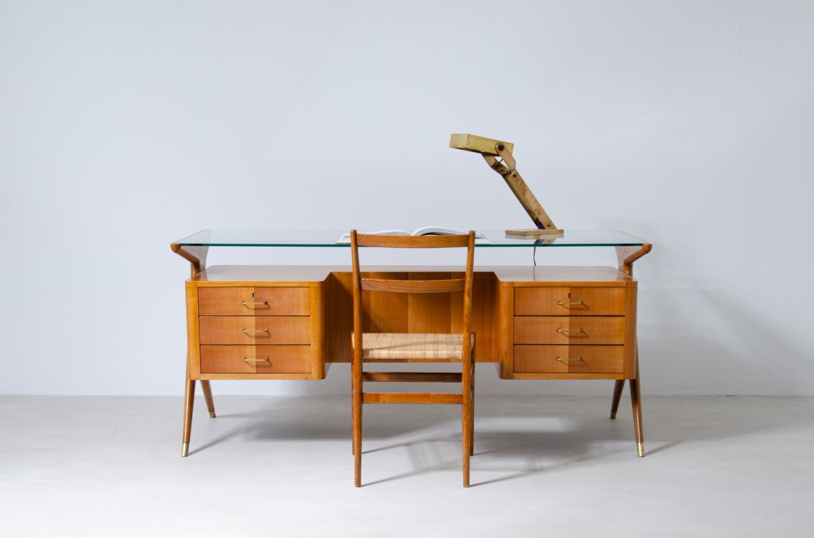 Scrivania in legno biondo con piano in vetro di grande spessore e montanti laterali sagomati con puntali in ottone,.  Manifattura italiana 1950ca.