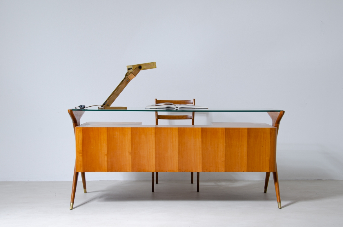 Scrivania in legno biondo con piano in vetro di grande spessore e montanti laterali sagomati con puntali in ottone,.  Manifattura italiana 1950ca.