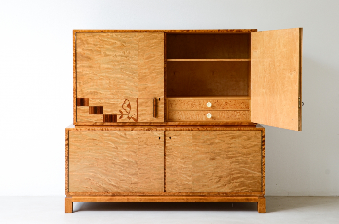 Mobile contenitore nello stile di Axel Einar Hjort, in acero marezzato con intarsi Art Deco sul fronte. All'interno ripiani e cassetti con pomoli in galalite.  Svezia  1930 ca.